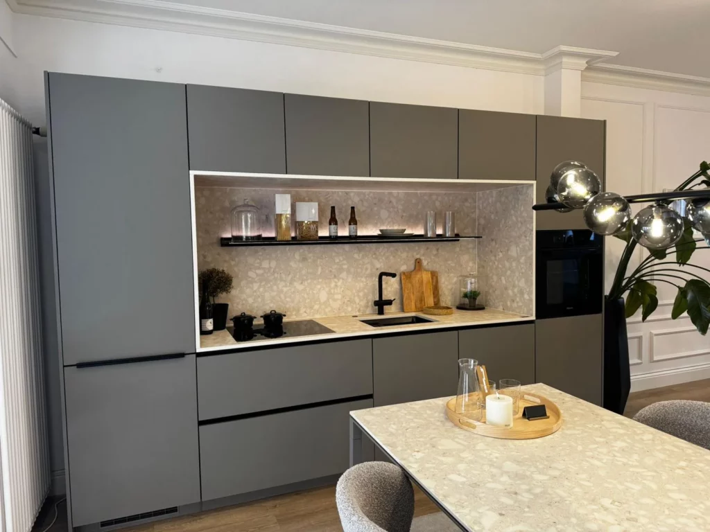 Einbaukühlschrank vollintegriert: taupegraue hochschrankzeile, links die zweigeteilte gerätefront mit schwarzer griffleiste und lüftungsgitter im sockel, rechts der backofen im HOCHSCHRANK