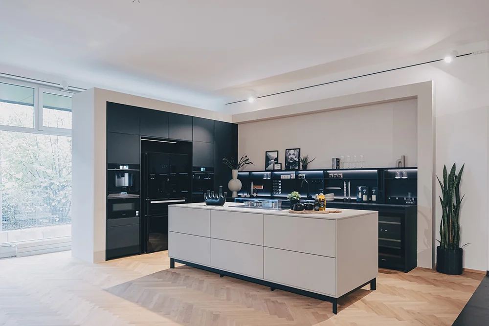 Küche farben im SHOWROOM Weinheim: schwarze hochschrankwand mit geräten und eine KOCHINSEL in hellem sandton auf fischgrätparkett