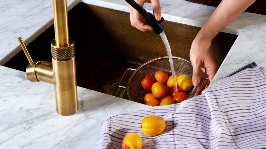 Quooker wasserhahn in messing patina über einer spüle in einer marmor-ARBEITSPLATTE, aprikosen werden in einem sieb abgespült